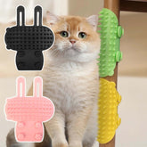 Cat Hair Removal Massage Comb in pink, black, and green with a cozy cat looking on.