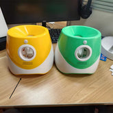 Lanzador automático de pelotas de tenis para perros en amarillo y verde sobre una mesa de madera, listo para jugar.