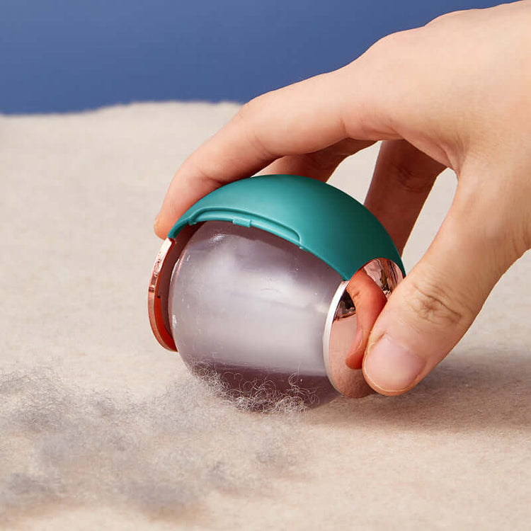 Person using a ball-shaped reusable lint roller to remove lint and pet hair from fabric.