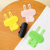 Colorful cat hair removal massage combs in yellow, pink, black, and green on a wooden table.