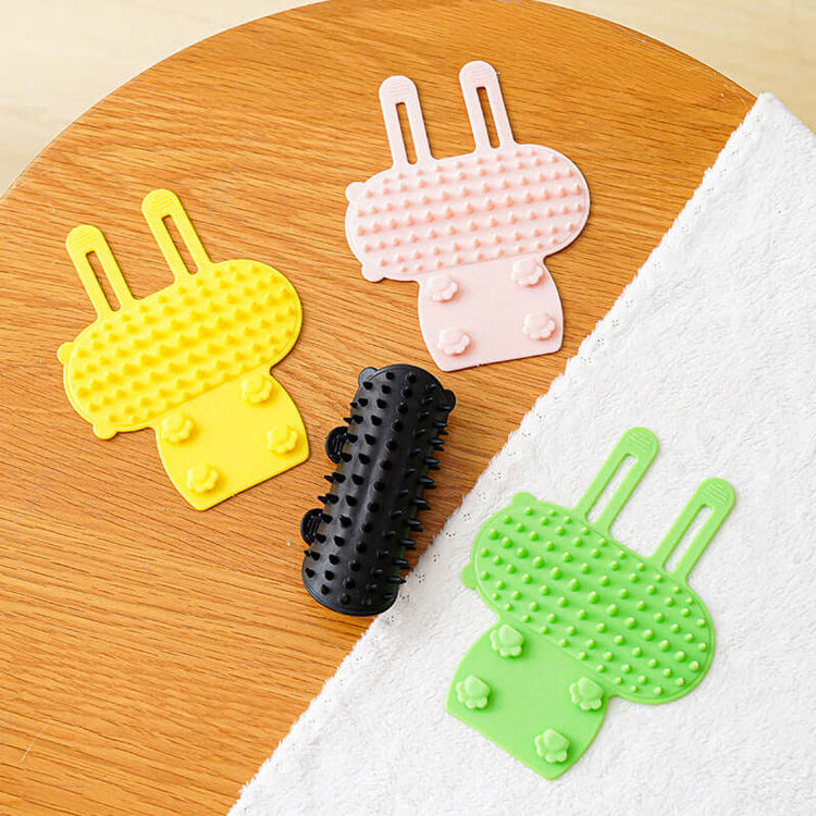 Colorful cat hair removal massage combs in yellow, pink, black, and green on a wooden table.