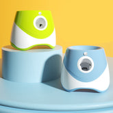 Lanzador automático de pelotas de tenis para perros en azul y verde, expuesto sobre un podio con fondo amarillo intenso.