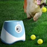 Lanzador automático de pelotas de tenis para perros sobre césped verde, con un perro y pelotas de tenis.